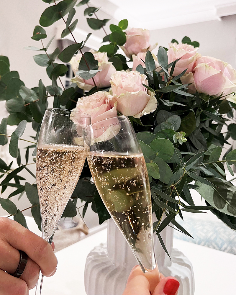 Two flutes of champagne clinking in front of a bouquet