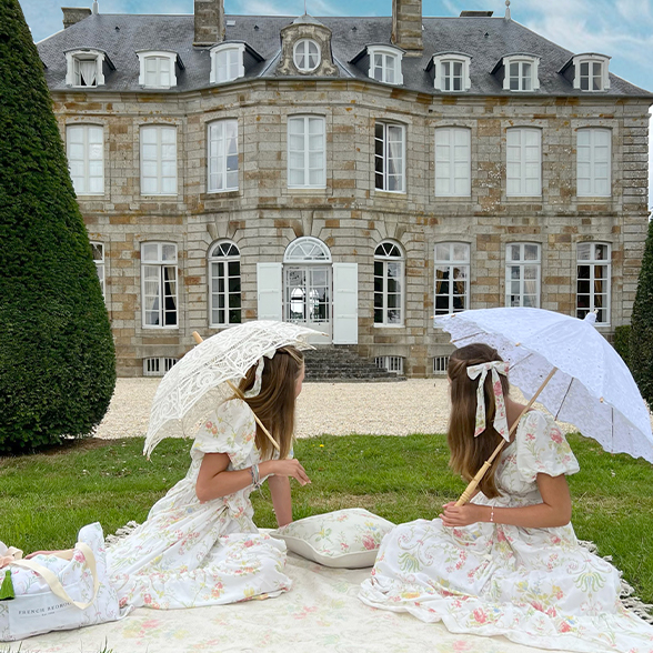 two girls on a picnic blanket with floral dresses and lace parasols