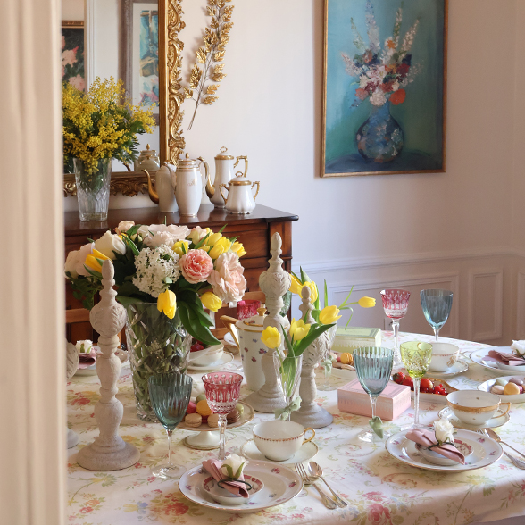 Spring themed tea. table set with floral table cloth, flowers and plates.