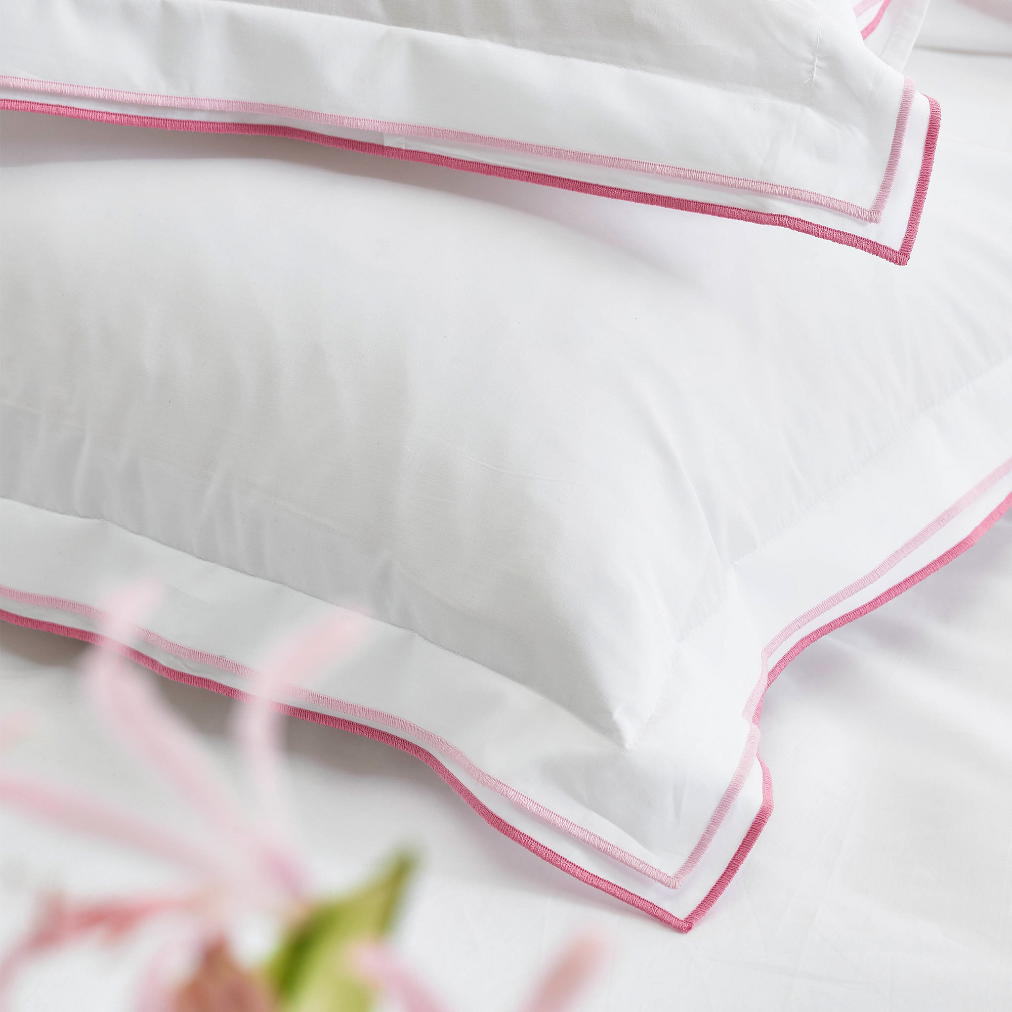 Close up image of the pillowcases in white with pink piped edging. Part of the Luxury cotton 400-thread count Designers Guild bed linen set.