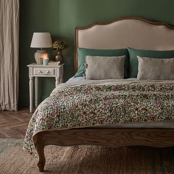 Upholstered wood bed styled with a quilted bedspread and complimentary cushions. 