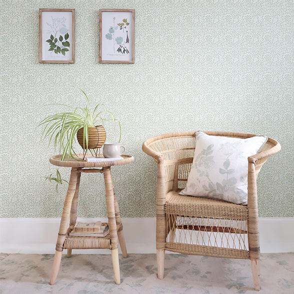 a rattan chair and rattan side table. The chair is styled with a cushion. While the side table has a potted plant and a cup of tea.